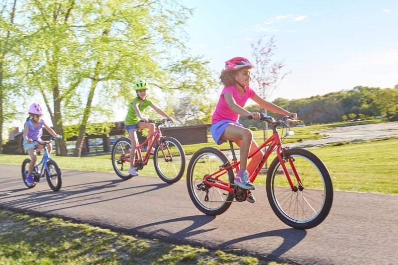 Trois enfants roulant joyeusement sur une piste cyclable sur des vélos pour enfant 24 pouces Trek