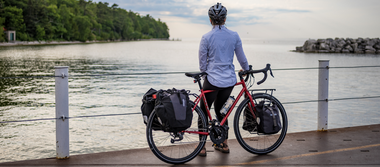 Cycliste assis sur le tube supérieur de son vélo devant un lac et qui regarde au loin 